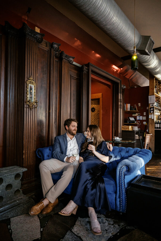 St. Louis engagement photos at Sasha’s on Shaw with couple sharing wine on blue velvet couch