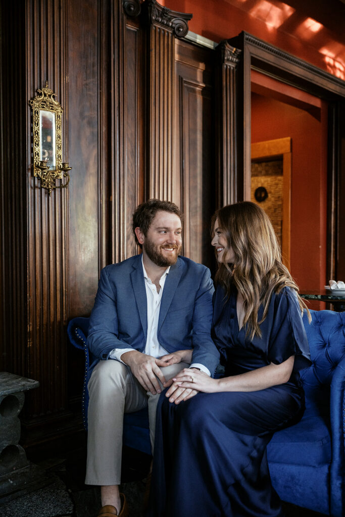 St. Louis engagement photos at Sasha’s on Shaw with couple sharing wine on blue velvet couch